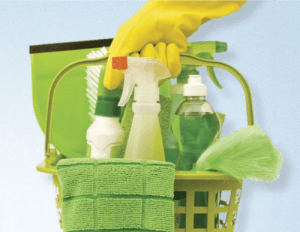A cleaning caddy with eco-friendly glass and surface cleaners, cloths and scrubbing brushes being held by a janitor with rubber gloves on.