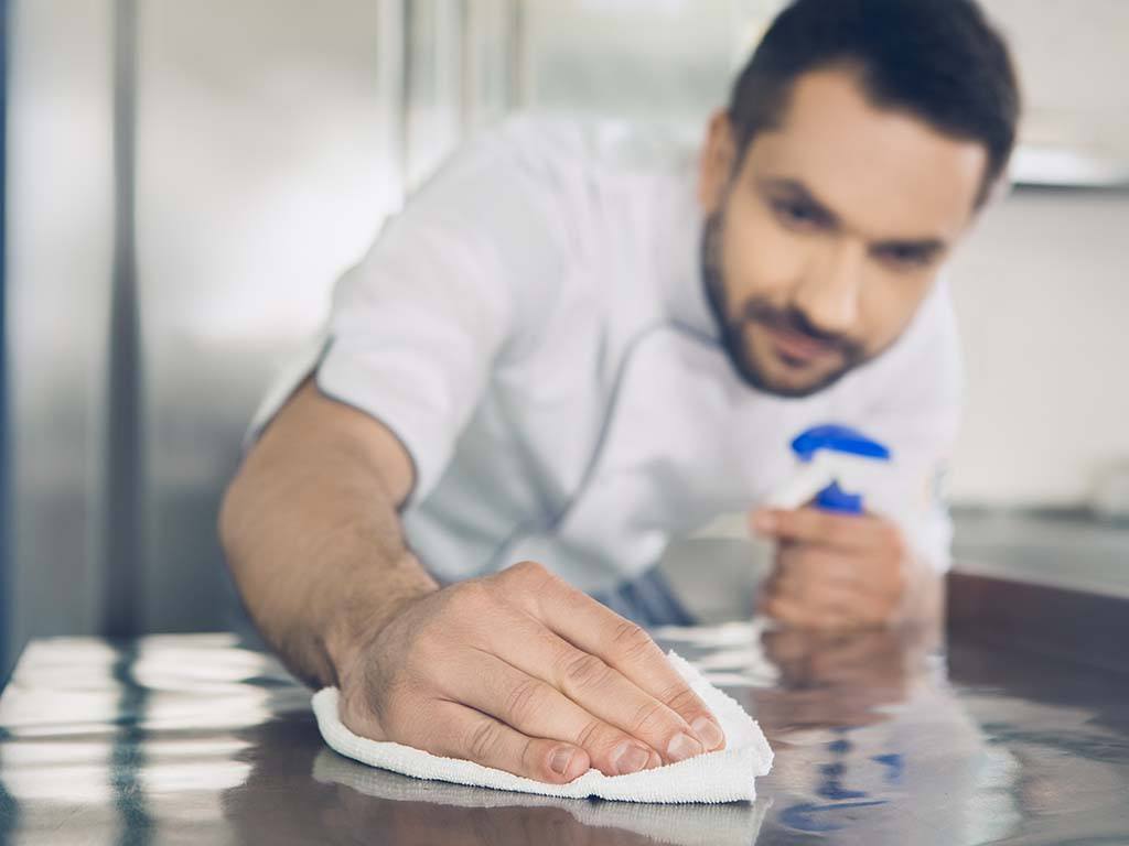 Man wiping down commercial kitchen counters with eco-friendly cleaning products.