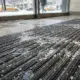 Close-up of a commercial scraper entrance mat covered in winter salt and melting snow in an NYC office building lobby.