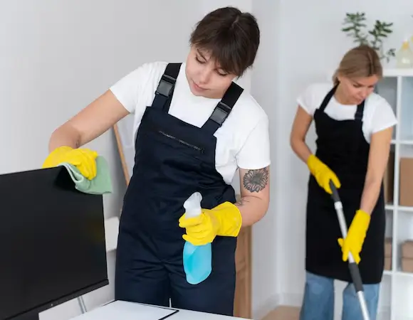 NYC green cleaning service worker wiping a computer monitor with a spray bottle and cloth, promoting eco-friendly janitorial services.