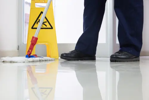 Close-up of mopping near a safety sign on a highly reflective surface. Expert commercial floor maintenance services in NYC.