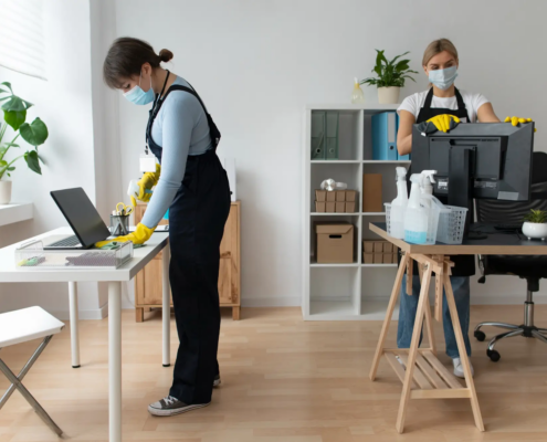 Janitorial staff sanitizing a desktop computer and laptop, demonstrating safe and secure office cleaning practices for businesses.