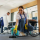 Two-person crew in blue aprons cleans floors and desks in an open office, showing what to expect from a commercial cleaning service provider in NYC.